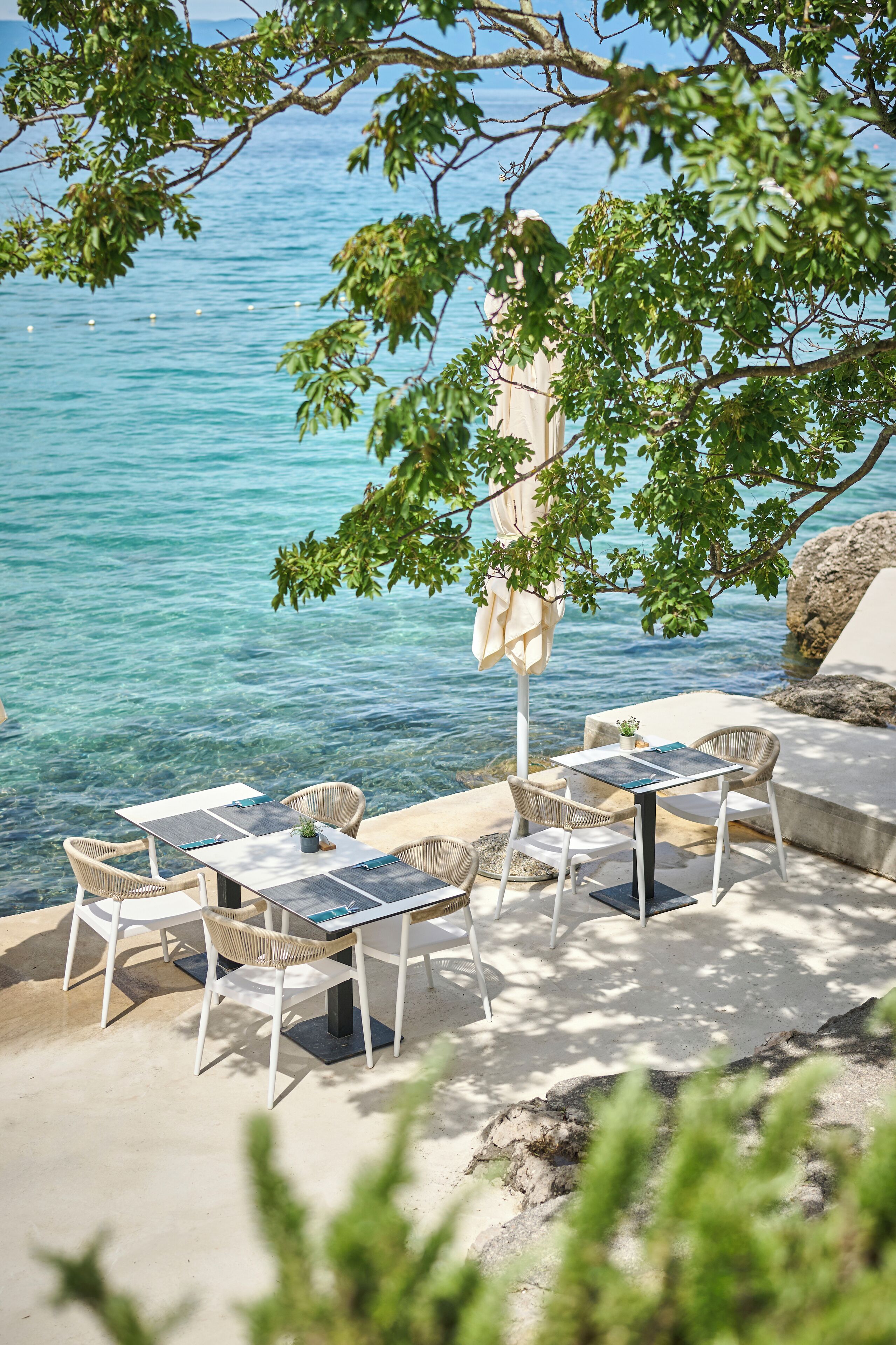 A seaside patio with tables and chairs, overlooking the sea.