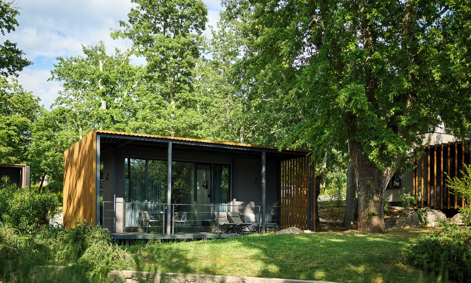 A modern outdoor structure with a glass enclosure, seating area, and a wooden facade.