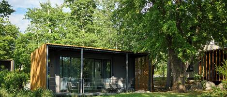 A modern outdoor structure with a glass enclosure, seating area, and a wooden facade.