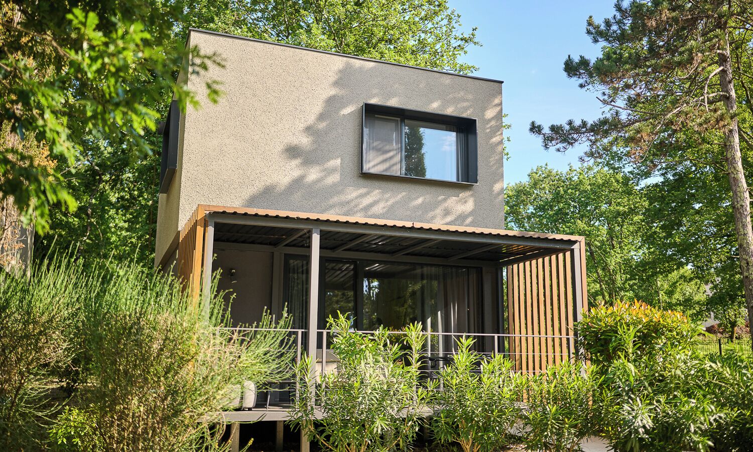 Un edifici modern de dues plantes amb un balcó, envoltat de vegetació abundant.