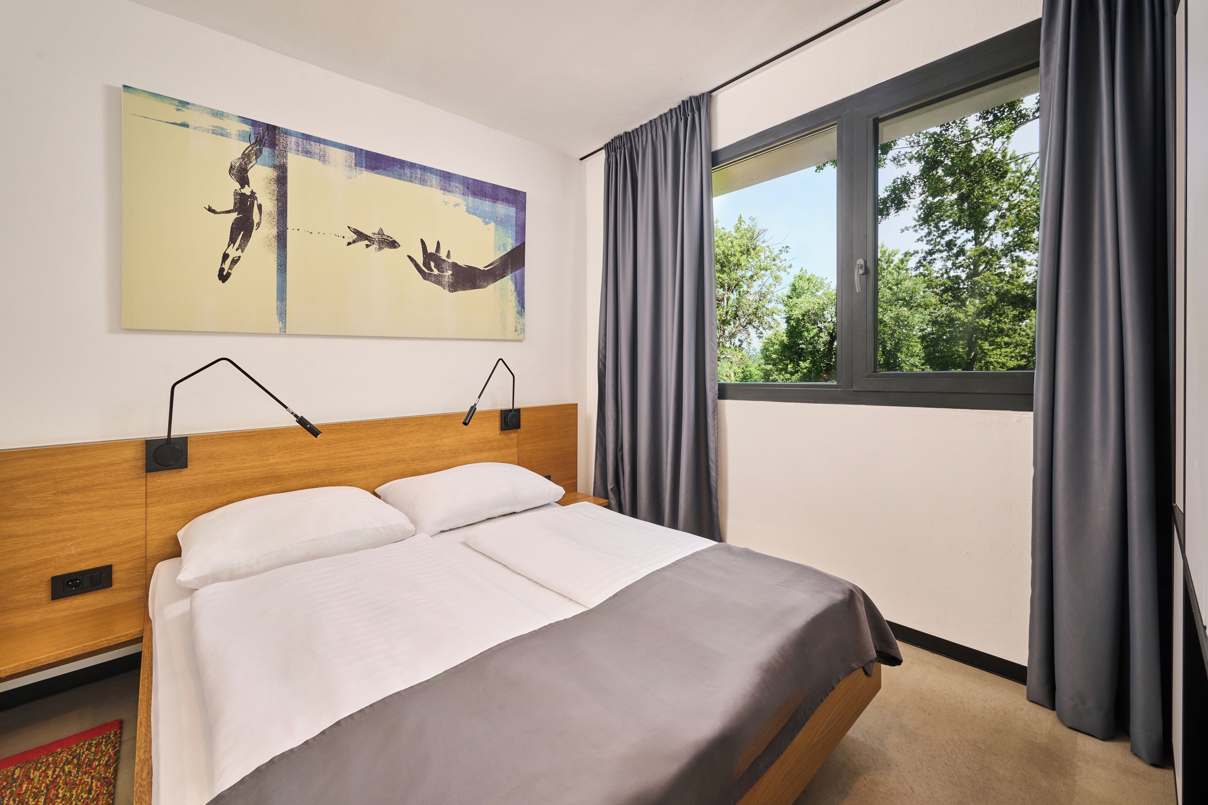 Ein modernes Hotelzimmer mit einem großen Bett, einem Telefon an der Kopfteil, einem Fenster mit Vorhängen und einem Bild an der Wand.