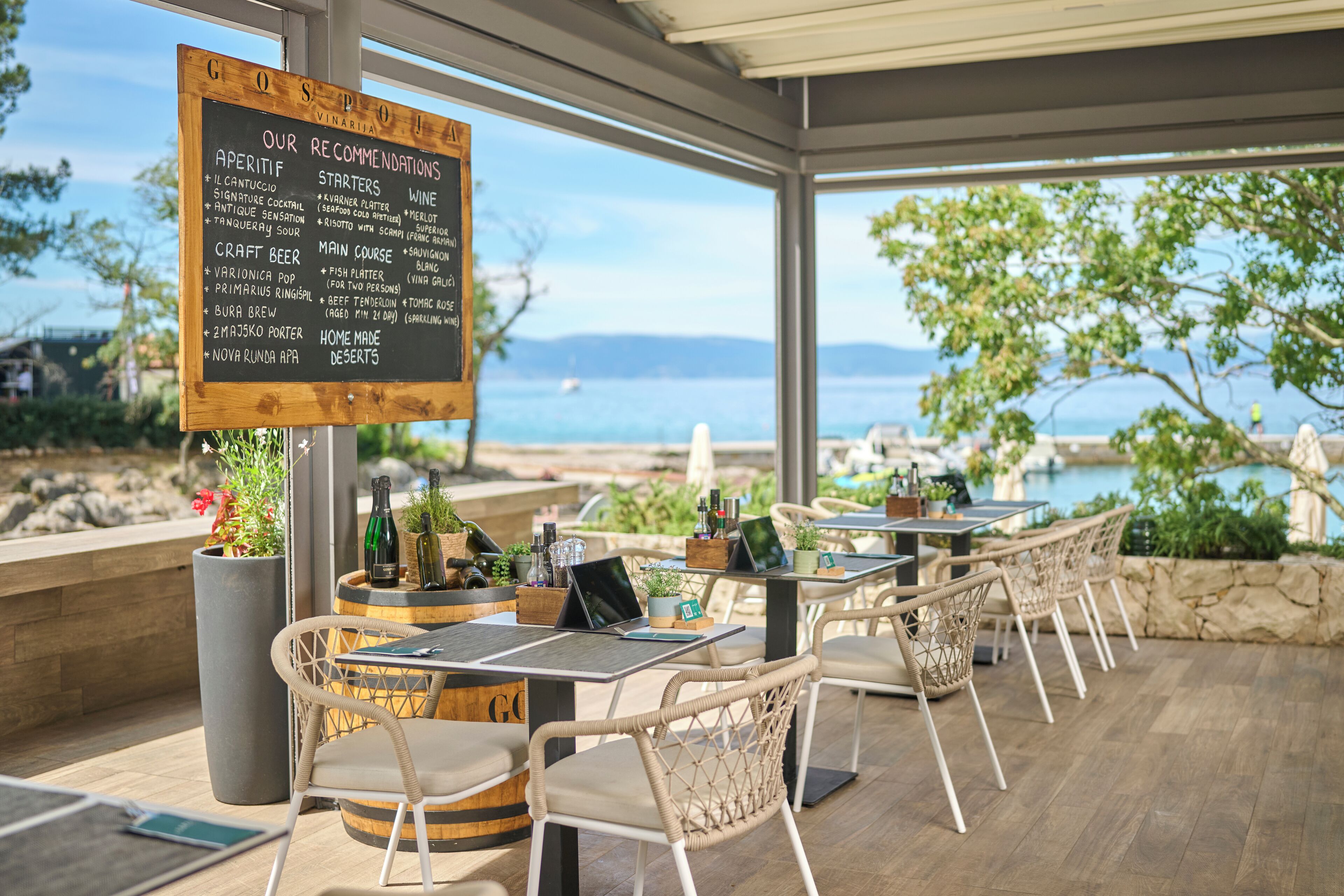 Un espace extérieur aménagé avec des tables et des chaises, un panneau affichant le menu et une vue sur la mer.