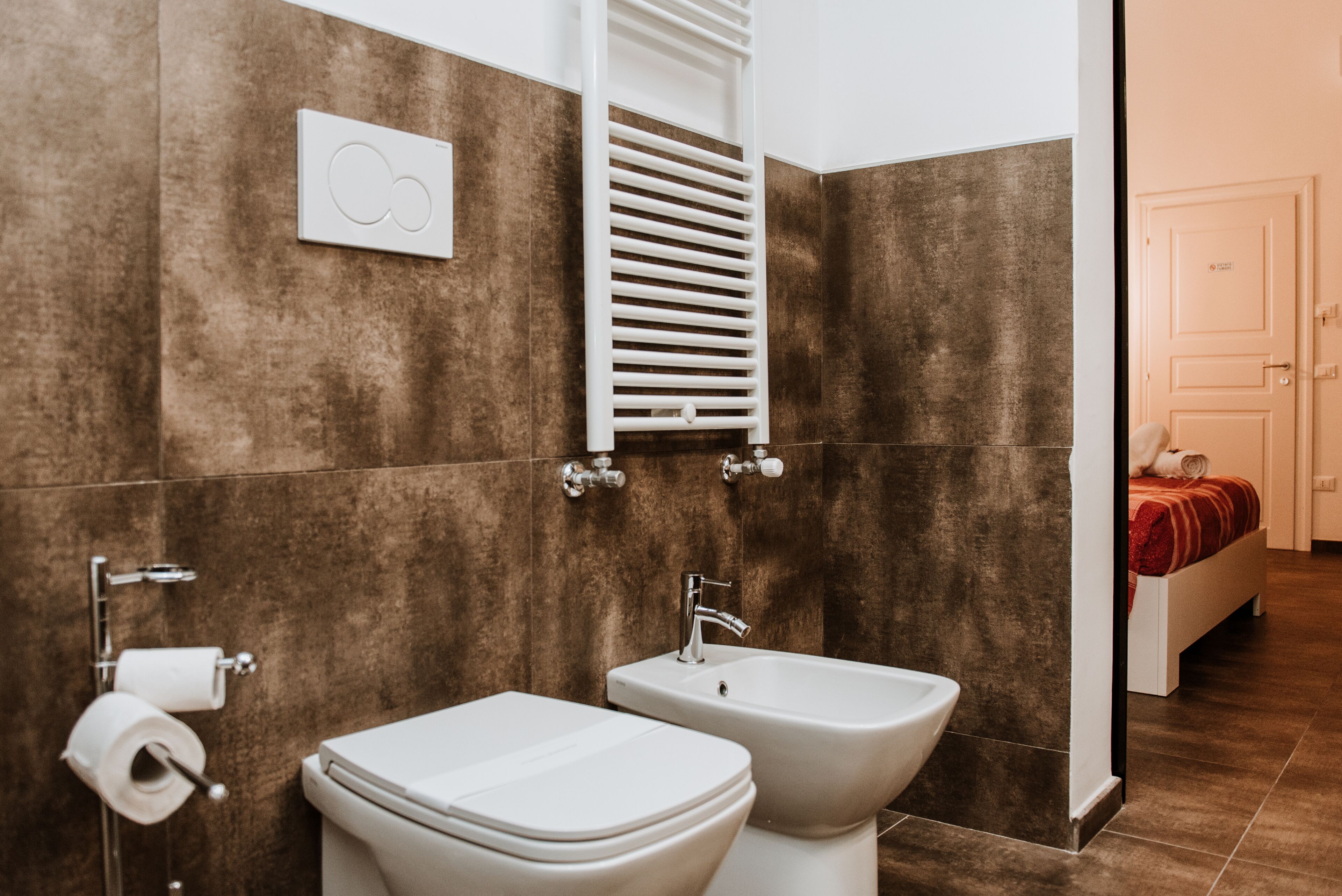 A modern bathroom with a toilet, bidet, and towel rack.