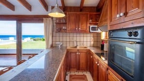 A kitchen with wooden cabinets, a black oven, and a view of the ocean. - Directly by the sea with greenhouse - Villa Solivent (Mercadal)