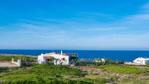 A coastal property with a white building, a view of the sea, and green vegetation. - Directly by the sea with greenhouse - Villa Solivent (Mercadal)