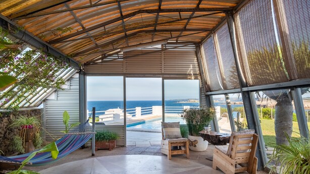 A covered patio with a view of the ocean, a hammock, and wooden seating. - Directly by the sea with greenhouse - Villa Solivent (Mercadal)