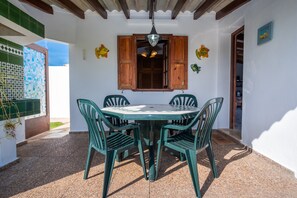 Une table ronde entourée de quatre chaises, une fenêtre en bois avec des volets et un luminaire suspendu.