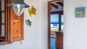 A room with a wooden door, a hanging light fixture, and a view of the sea through an open door. - Directly by the sea with greenhouse - Villa Solivent (Mercadal)