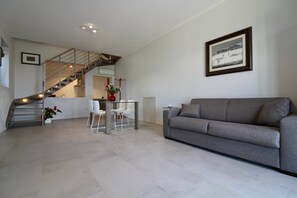 Un salon moderne avec un canapé gris, un escalier, un coin repas avec des chaises et un tableau encadré au mur.