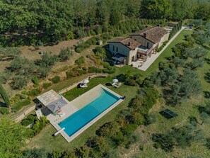 Vista aérea de uma propriedade com piscina, área de pátio e uma casa grande rodeada por vegetação.