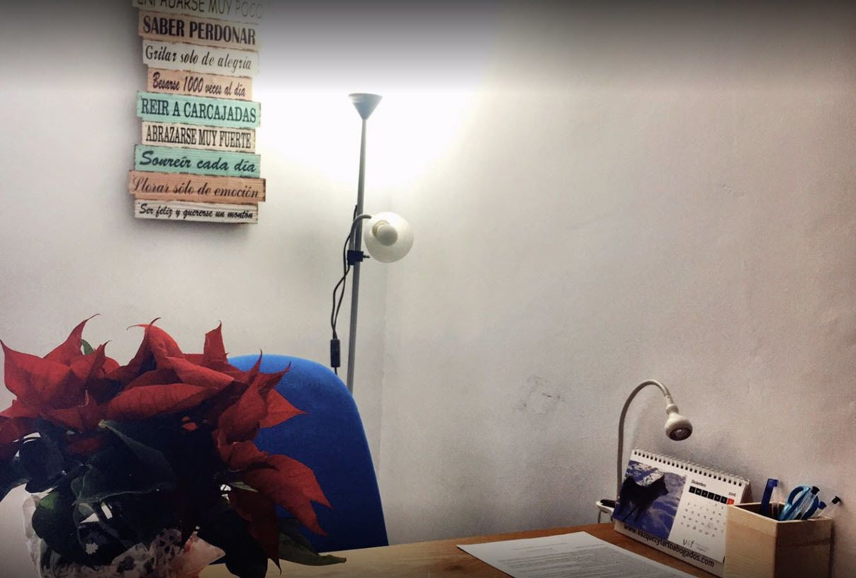 A room with a desk, a chair, a lamp, a calendar, and a vase with red flowers.