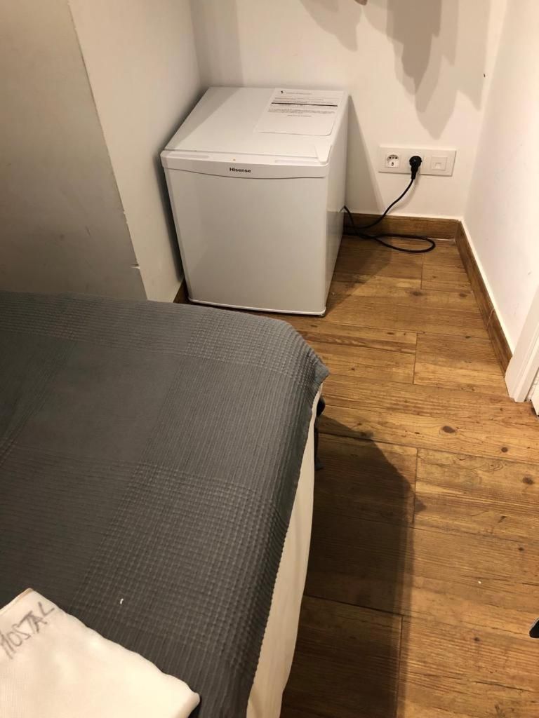 Una habitación con cama, un calentador blanco y suelo de madera.