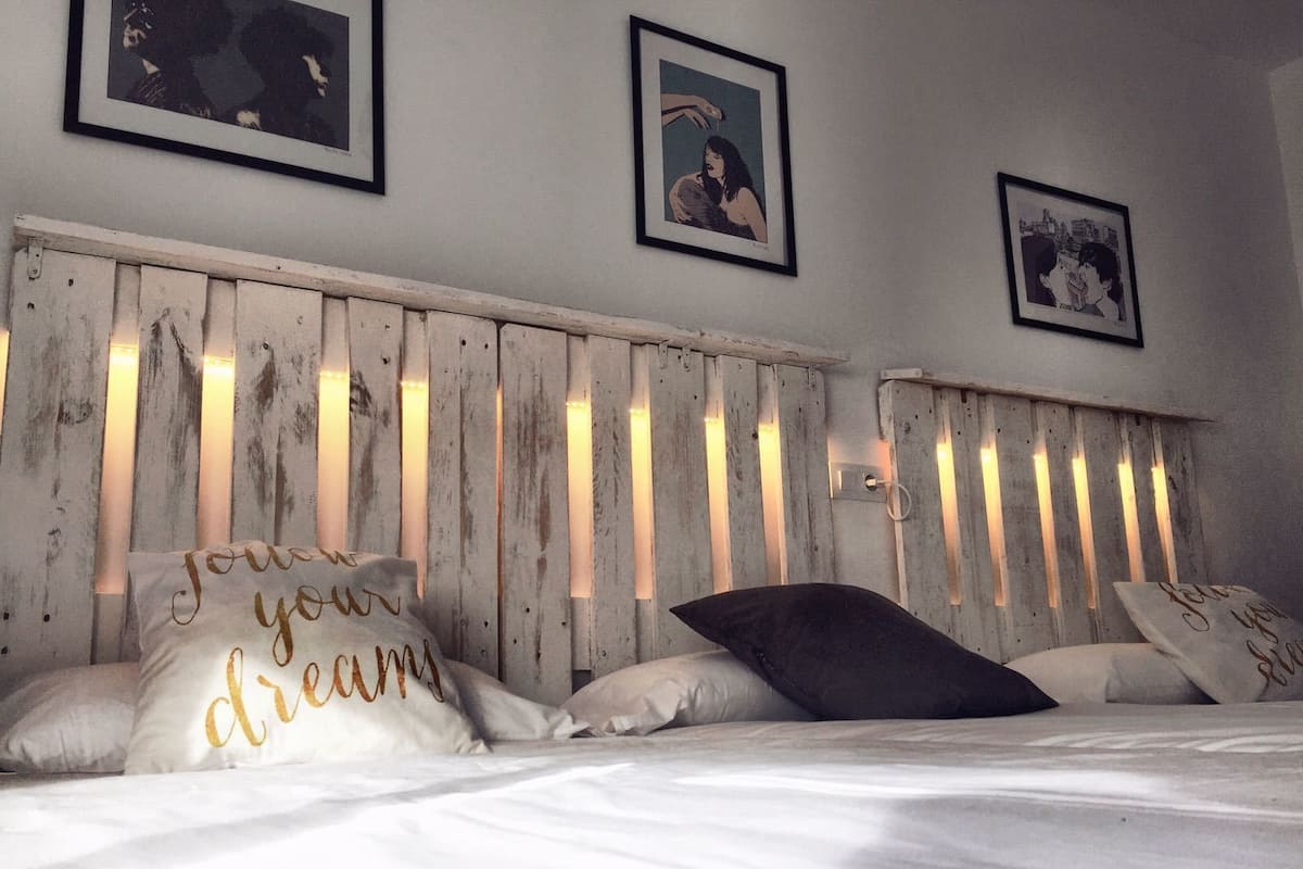 Een slaapkamer met een houten hoofdbord, wit beddengoed en decoratieve kussens met tekst.