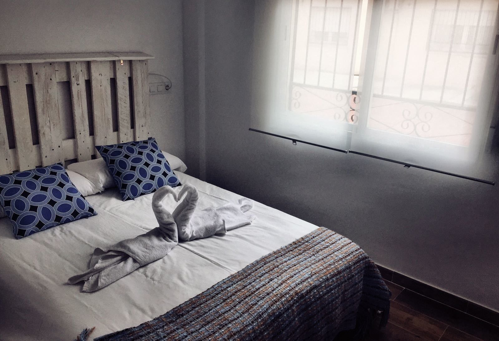 A neatly made bed with a heart-shaped towel, two patterned pillows, and a woven throw blanket.