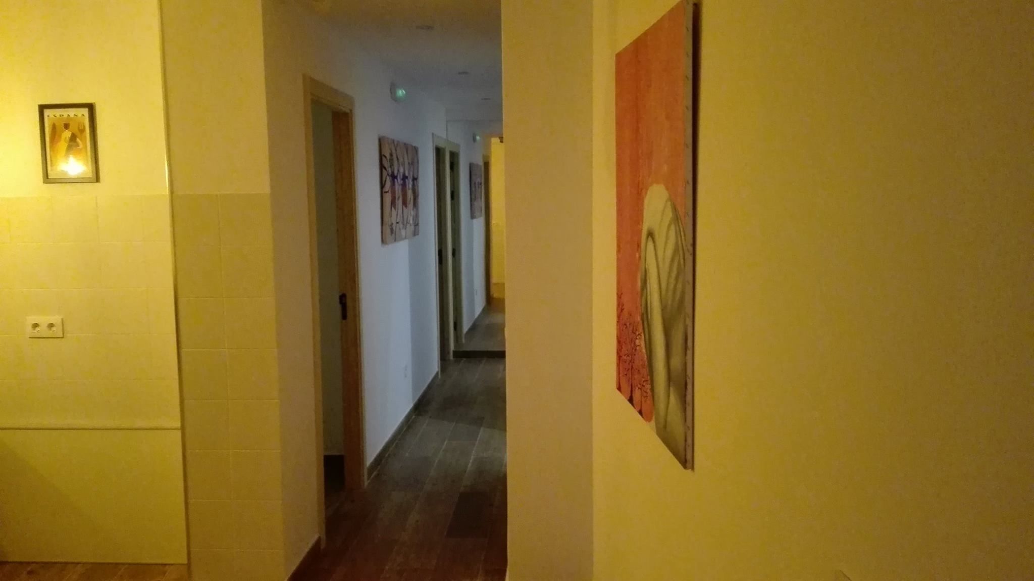 Un pasillo con paredes amarillas, piso de baldosas y obras de arte enmarcadas.