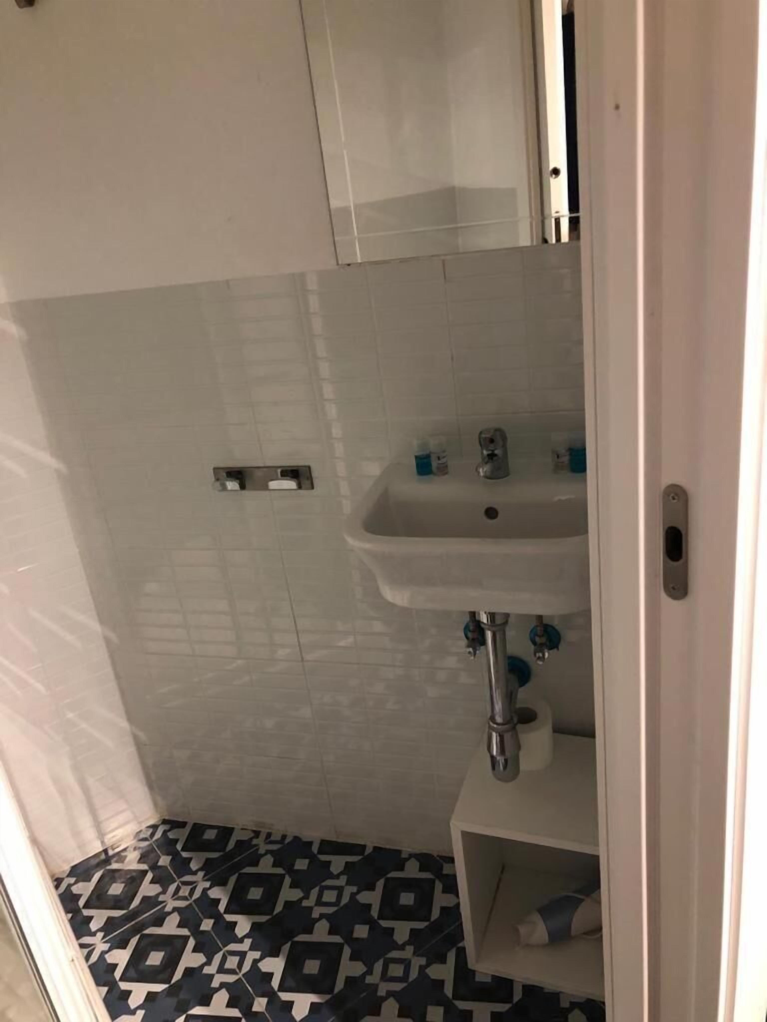 Un baño pequeño con un lavamanos blanco, un espejo encima y un suelo estampado.