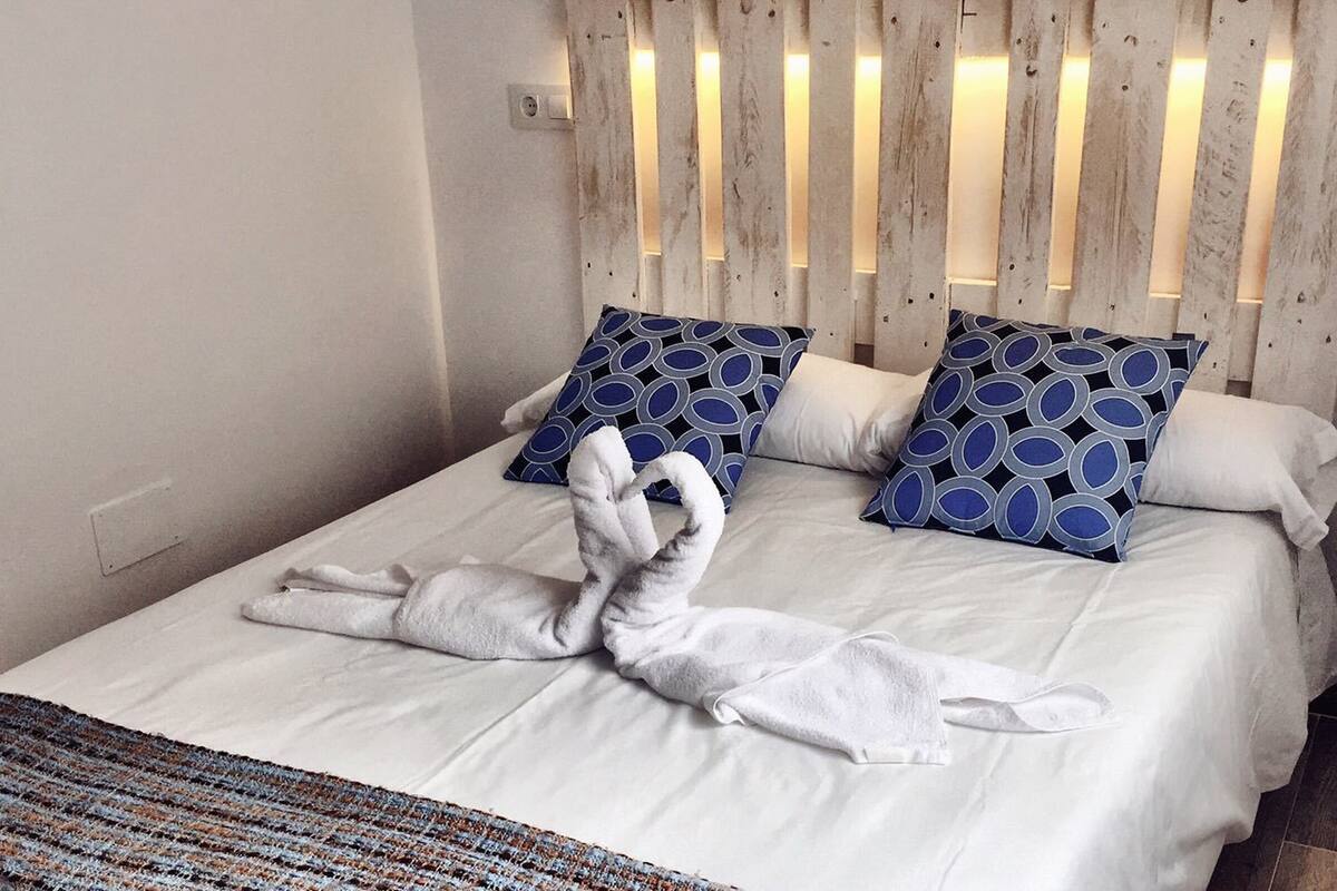 Een keurig opgemaakt bed met twee handdoeken gevouwen in de vorm van zwanen, een gestreept kussen en een houten hoofdbord.