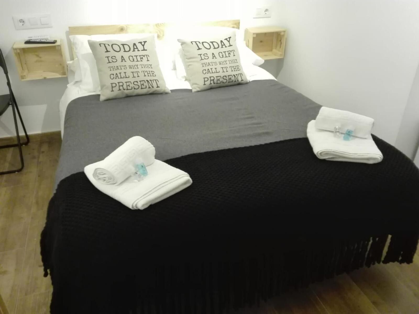 A neatly made bed with two pillows, a black bedspread, and two folded towels on the bed.