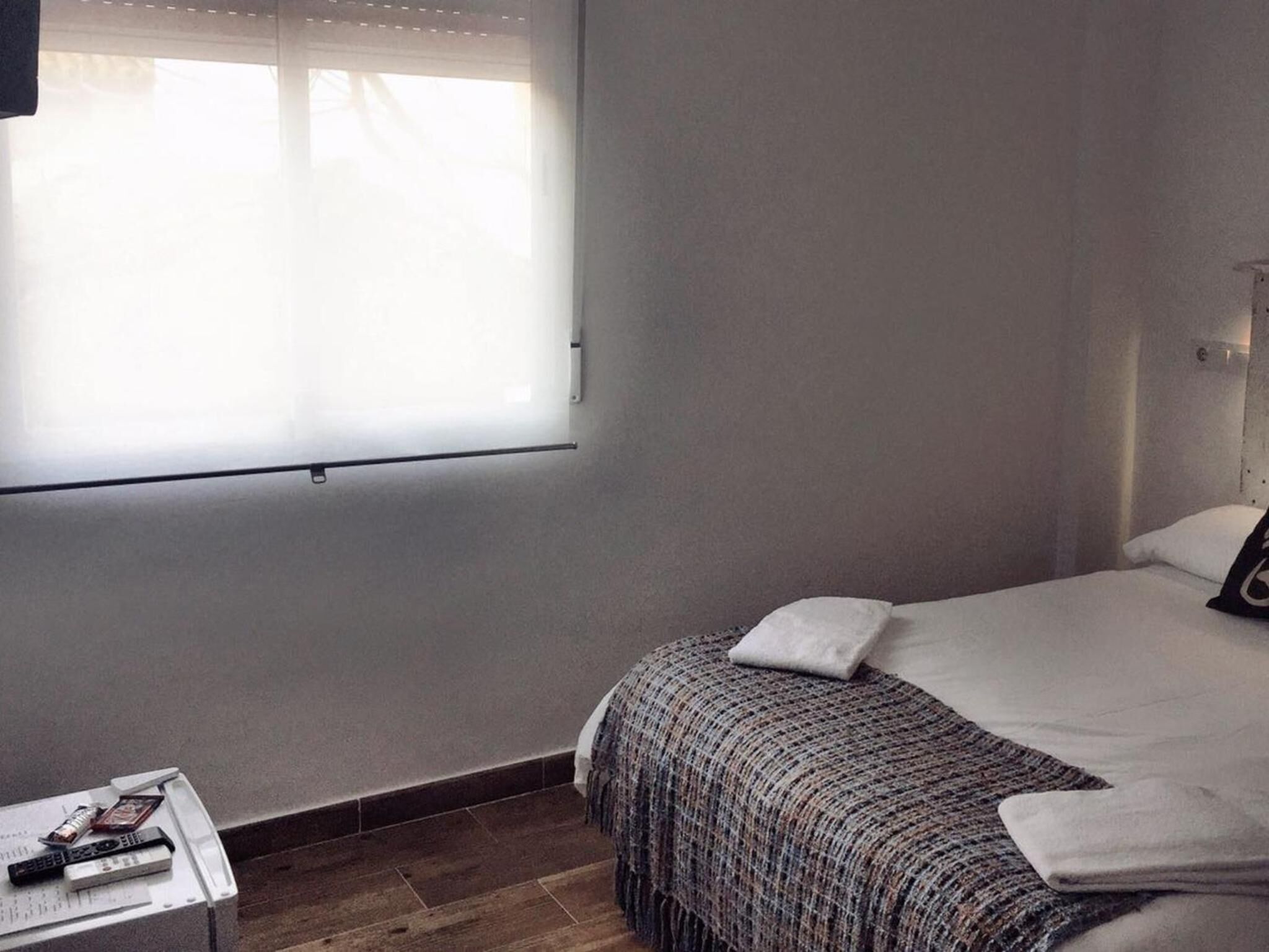 Quarto com uma cama, mesa de cabeceira e janela com persianas.