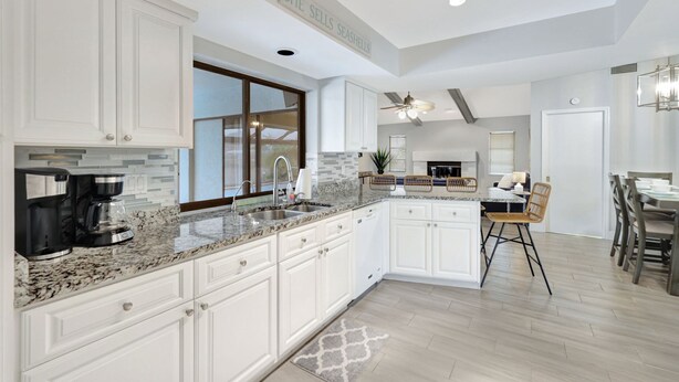 A modern kitchen with white cabinets, granite countertops, and a built-in island. - Canal fun! Boat, Pool, Hot tub, Bikes & Kayaks (Cape Coral)