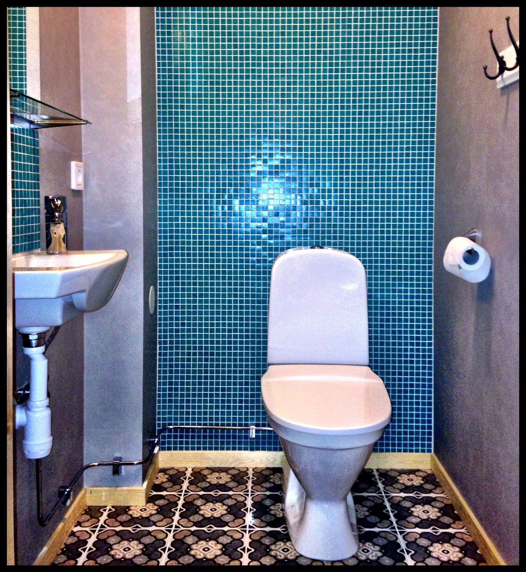 A bathroom with a toilet, sink, and blue tiled walls.