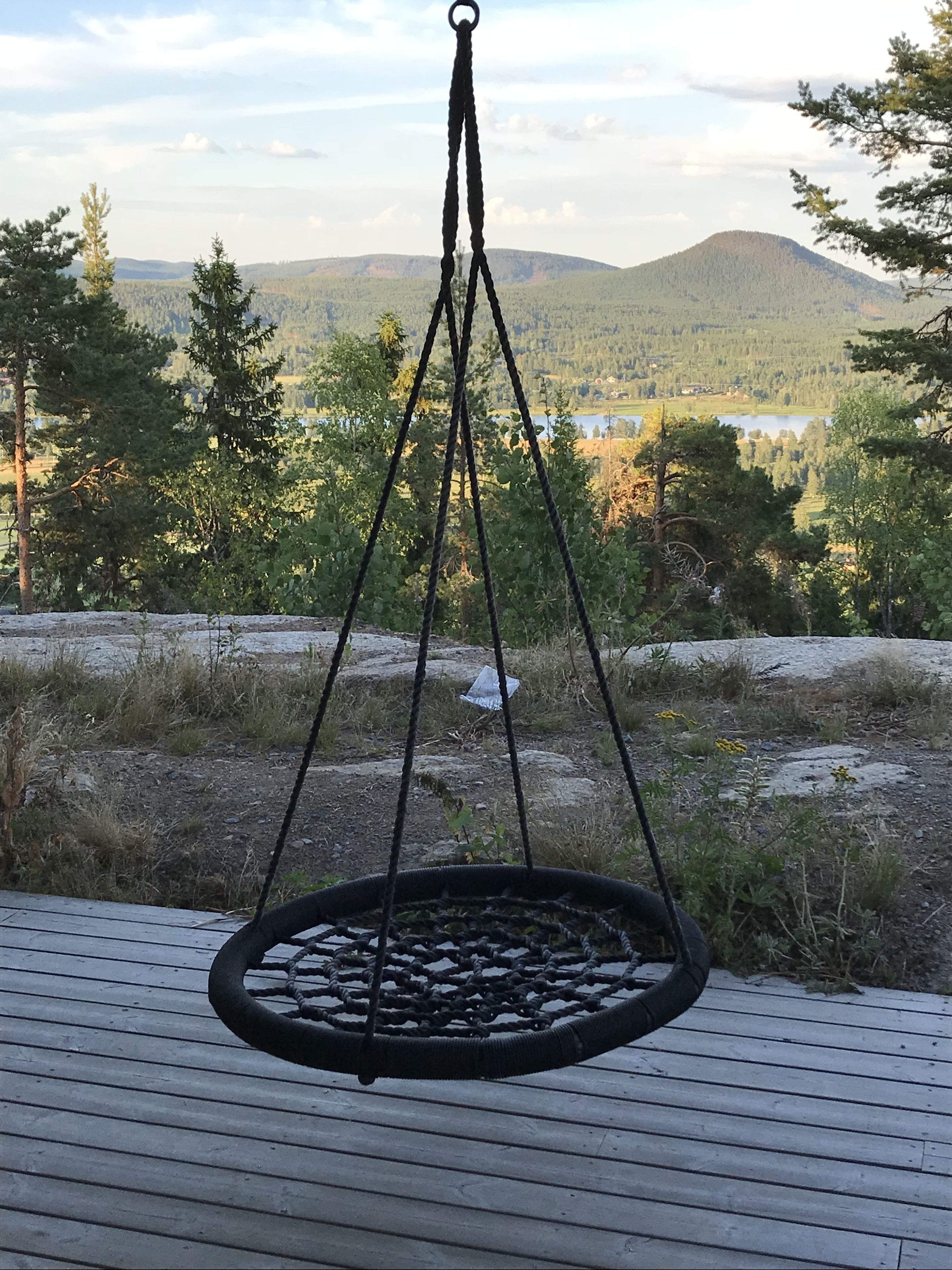Ein Hängesessel auf einer Holzterrasse mit Blick auf einen See und Berge im Hintergrund.