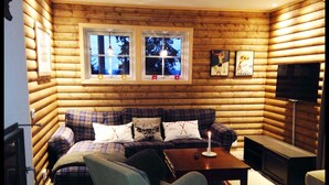 A cozy log cabin interior with a plaid sofa, a wooden coffee table, and a television on the right wall. - Alpstigen 8b (Jarvso)