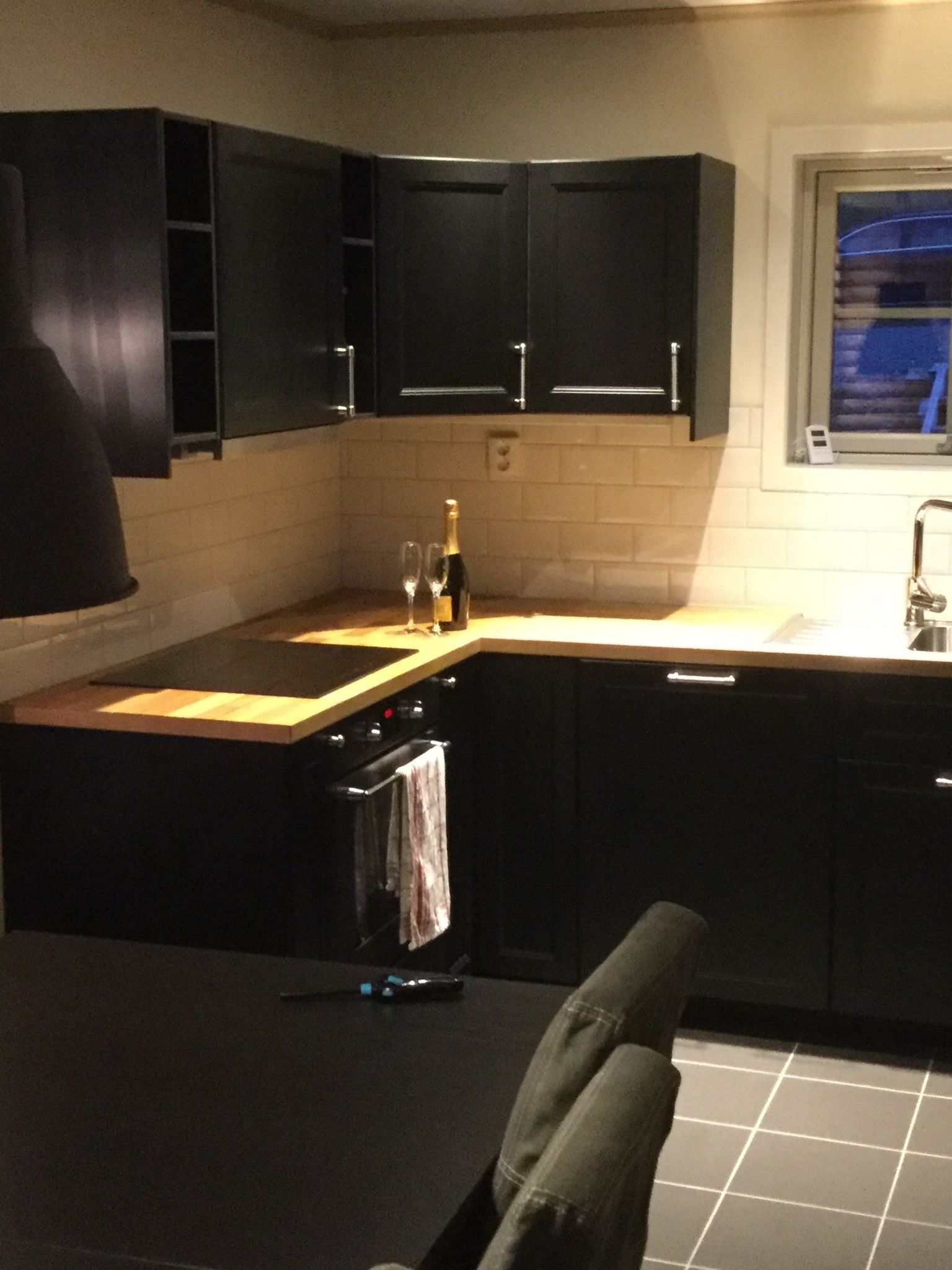 A kitchen with dark cabinets, a wooden countertop, a sink, and a window with a view.
