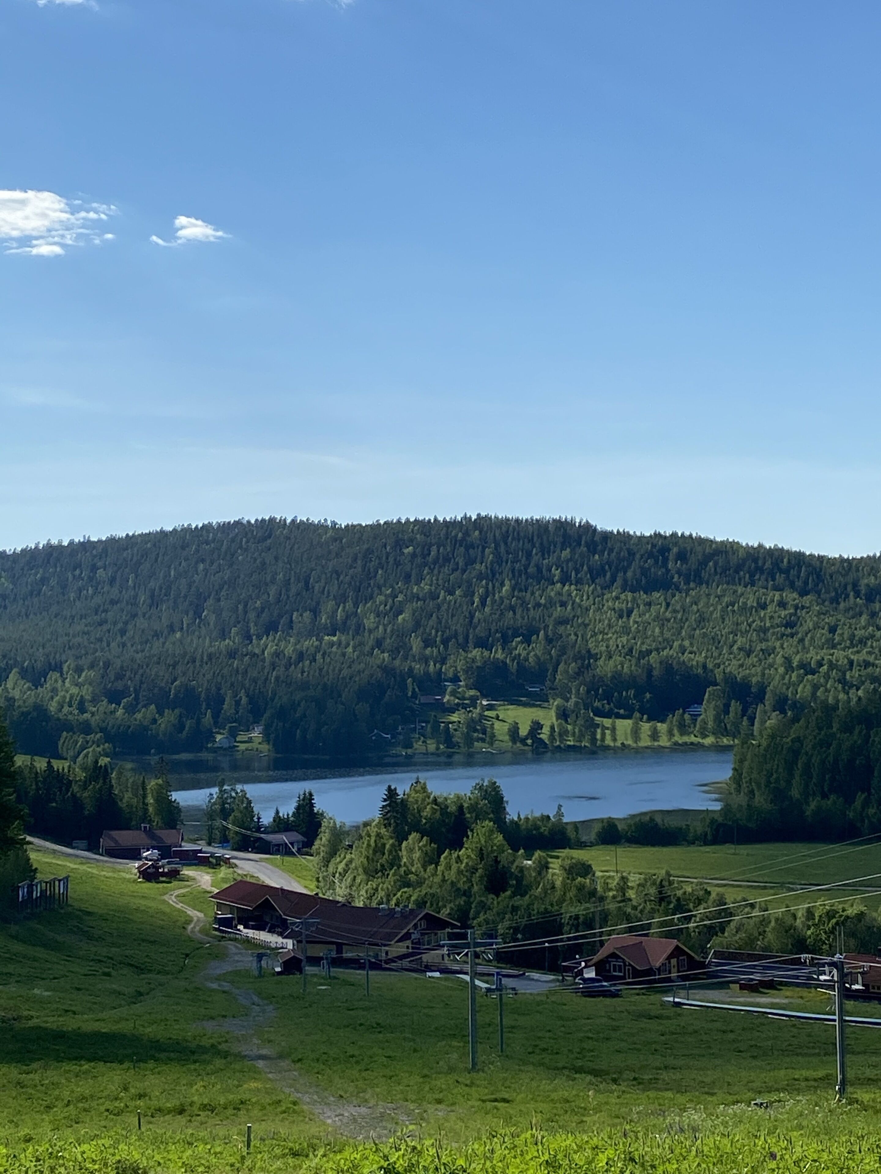 A rural landscape with a lake, forested hills, and a few houses.