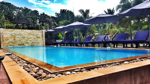 A swimming pool with lounge chairs and umbrellas, surrounded by a stone wall and tropical plants. - White Lotus Resort (Siem Reap)