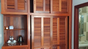 A wooden wardrobe with multiple compartments and a glass shower area visible through an adjacent door. - White Lotus Resort (Siem Reap)