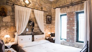 A stone-walled bedroom with a bed, curtains, a nightstand, a lamp, and a window. - Majestic Chateau - Spectacular Seascapes & Pool (Kalamata)