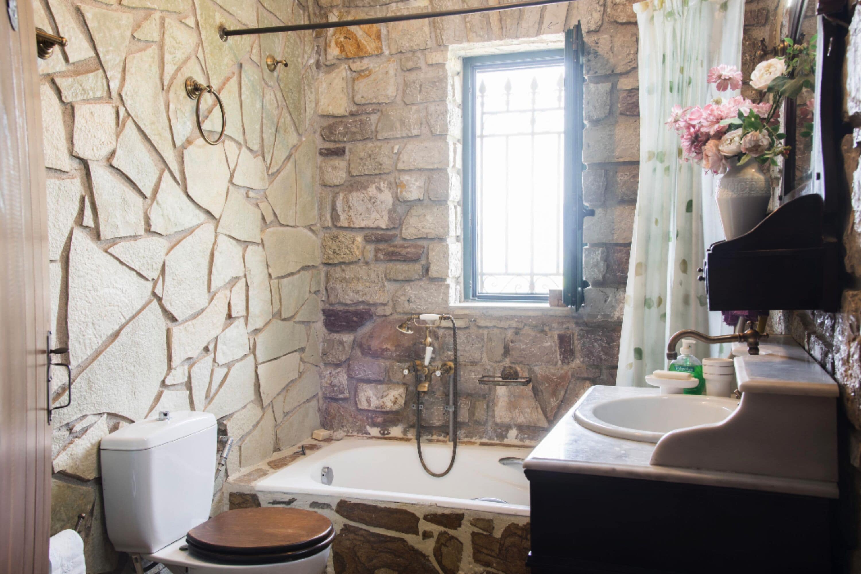 A bathroom with a stone wall, a bathtub, a toilet, and a sink.