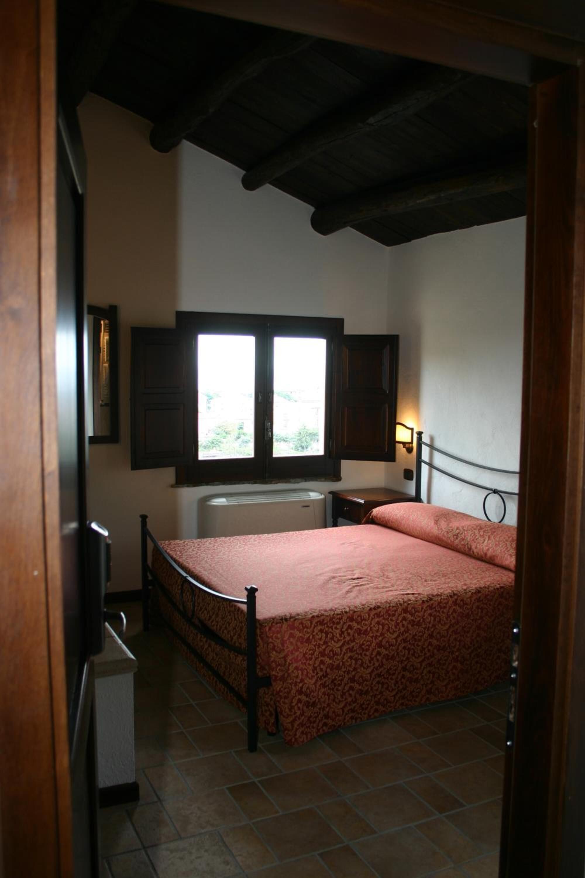 A bedroom with a bed, a window, a radiator, and a wall-mounted light fixture.
