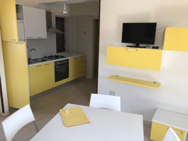 A compact kitchen with a dining area, a TV mounted on the wall, and a small table with chairs. - Borgo della Marinella (Amantea)
