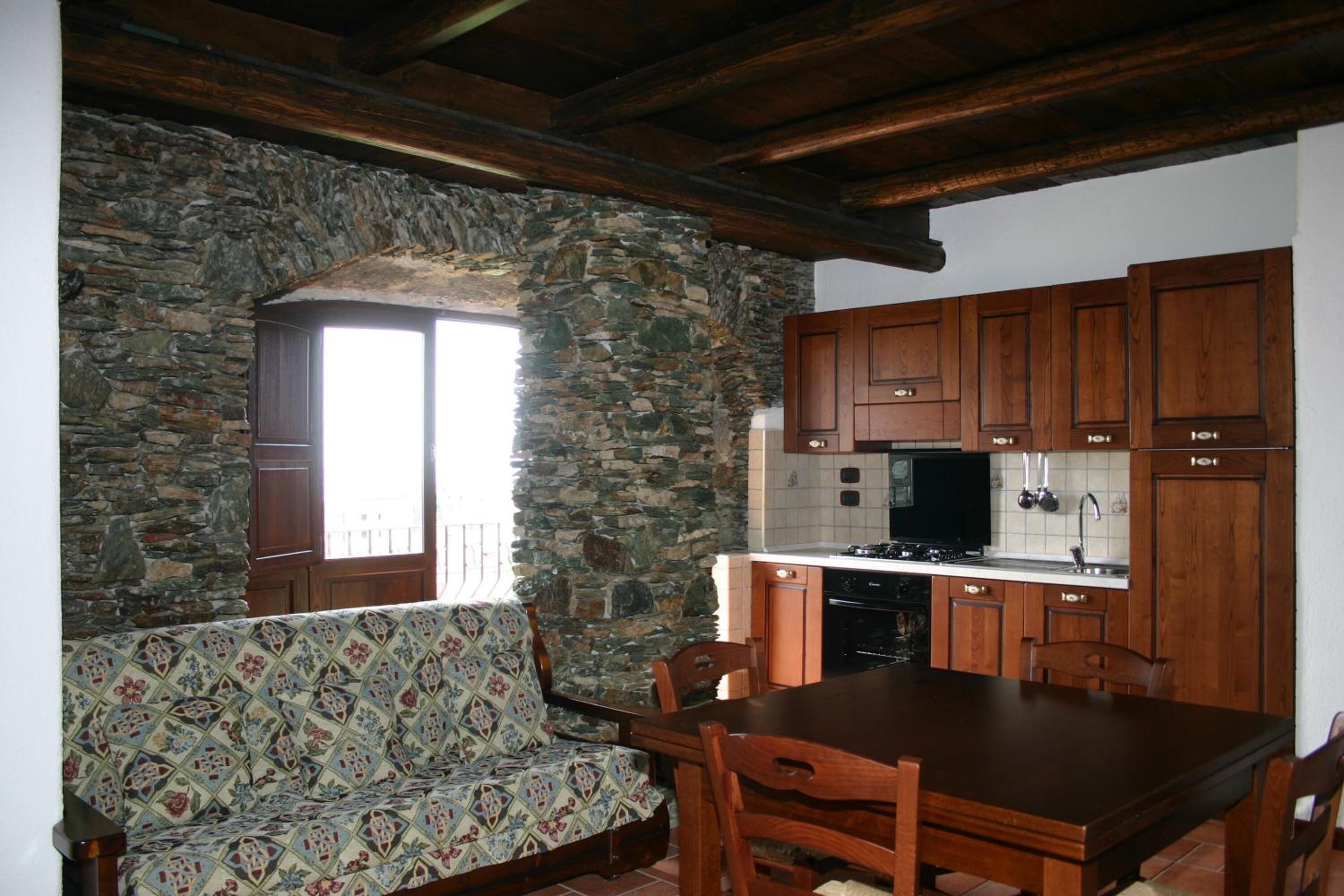 A cozy kitchen with stone walls, wooden cabinets, a dining table, and a patterned sofa.