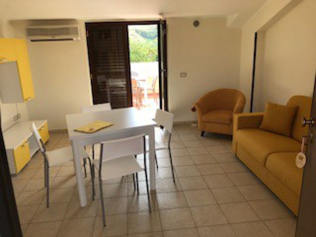 A room with a dining table, chairs, a sofa, and a sliding door leading to an outdoor area.