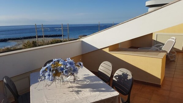 A balcony with a table set for two, a sofa, and a view of the ocean. - Borgo della Marinella (Amantea)