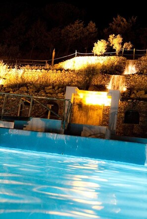Ein Pool mit Wasserfall, umgeben von einer Steinmauer und einem Holzzaun.
