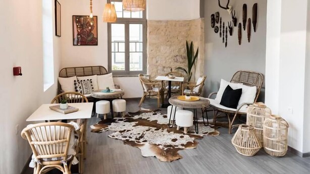 A cozy room with wicker furniture, a cowhide rug, and a wall decorated with antlers and tools. - Kumba Hostel (Chania)