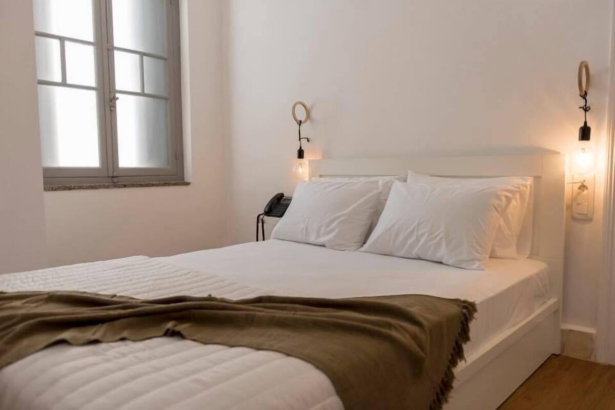 Quarto com cama, telefone ao lado da cama, janela e luminárias na parede.