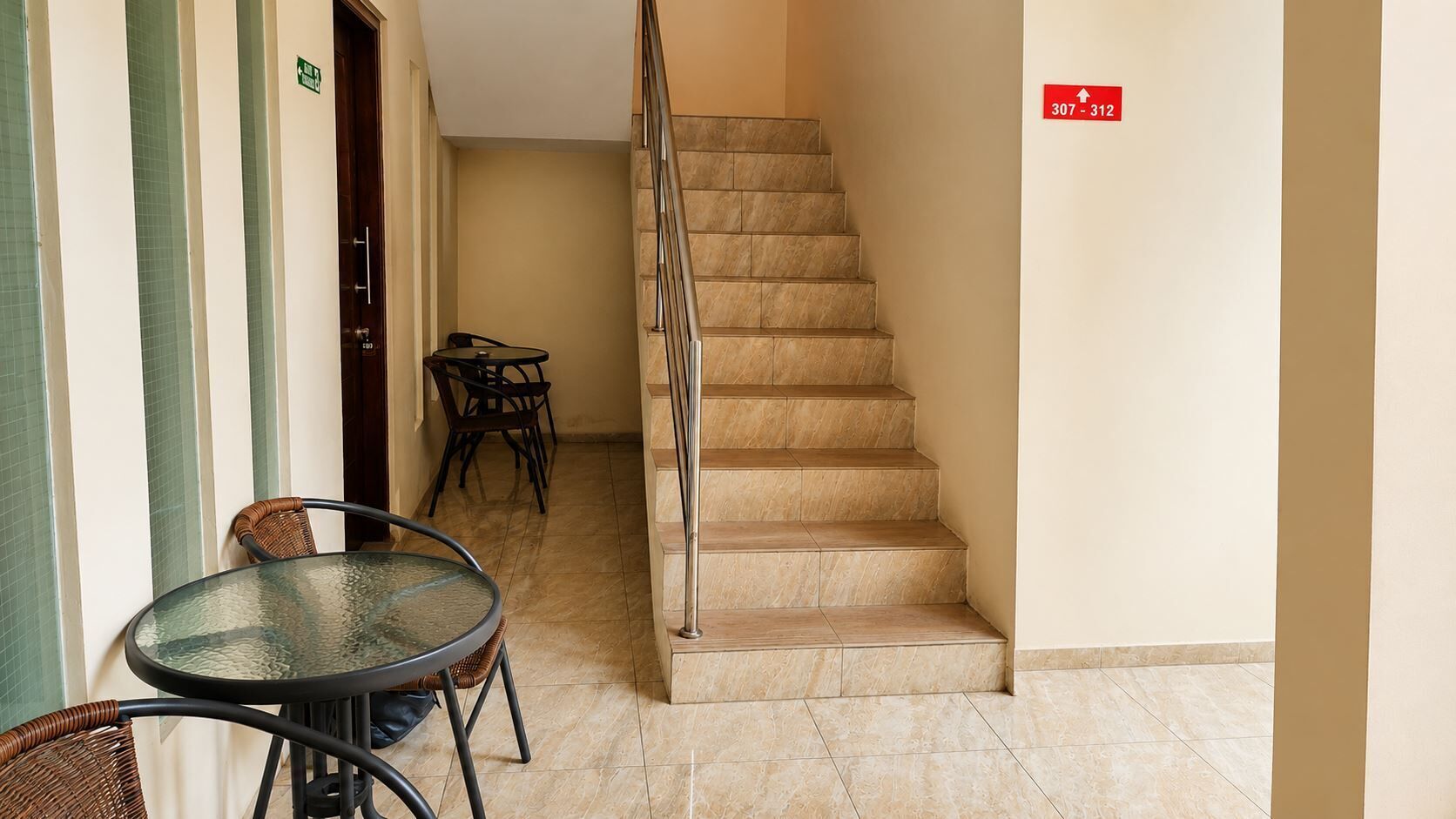Vestíbulo de hotel con una escalera, una mesa de cristal y sillas.