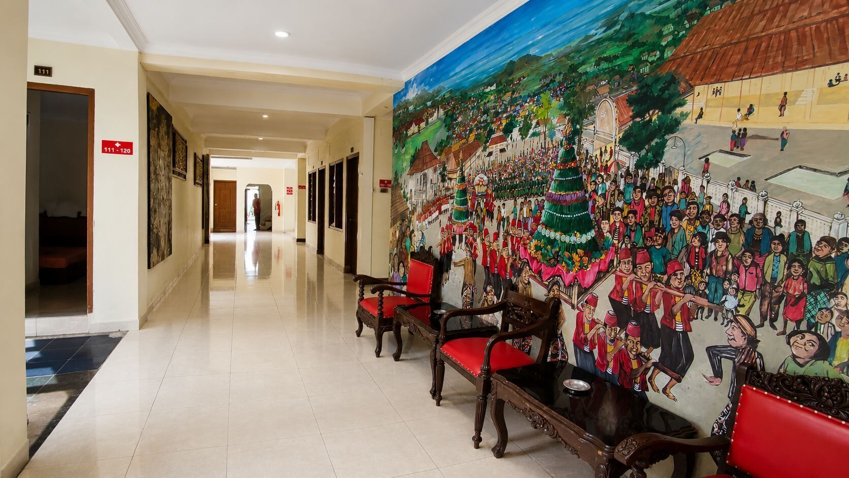 A hotel hallway with a mural, wooden chairs, and a tiled floor.