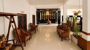 A spacious lobby with a reception desk, leather sofas, a wooden bench, and a statue. - Satya Graha Hotel (Yogyakarta)