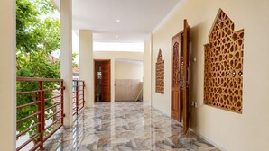 A hallway with a marble floor, wooden doors, and a red railing. - Satya Graha Hotel (Yogyakarta)