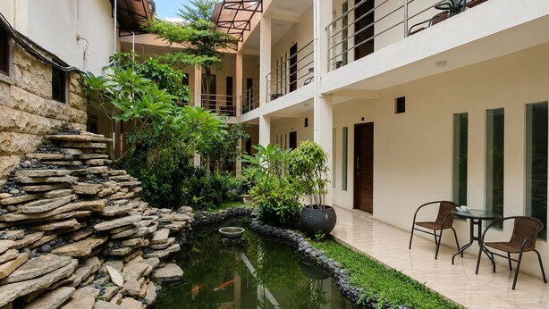 A courtyard with a koi pond, stone wall, potted plants, and outdoor seating. - Satya Graha Hotel (Yogyakarta)