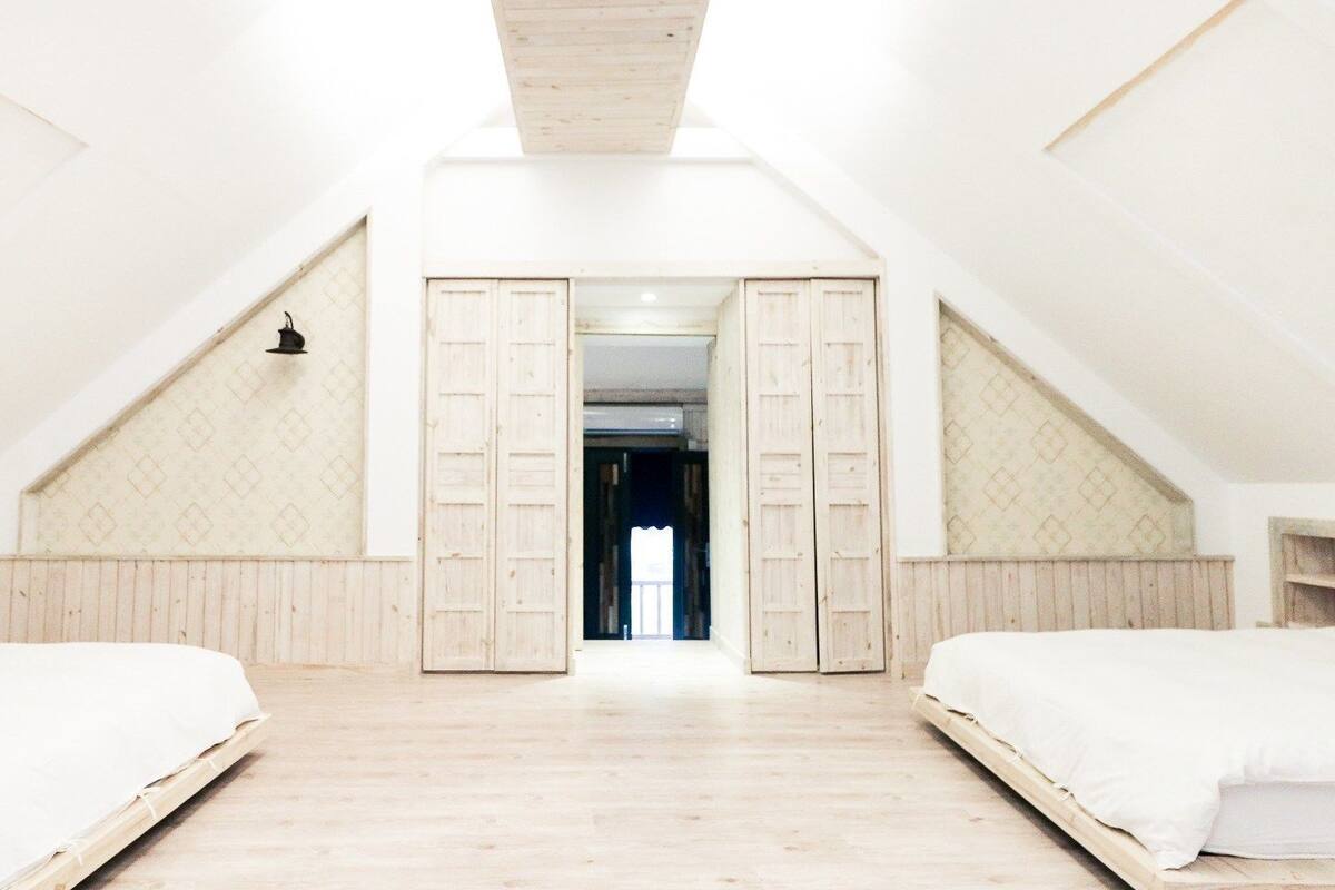 A room with two beds, wooden floors, and a sloped ceiling.