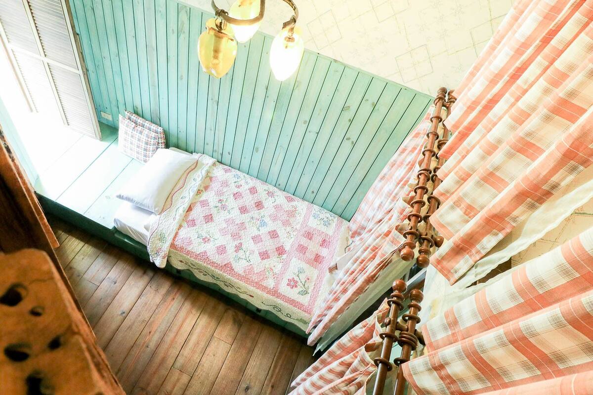 A small, cozy room with a bed, a wooden floor, and a window.