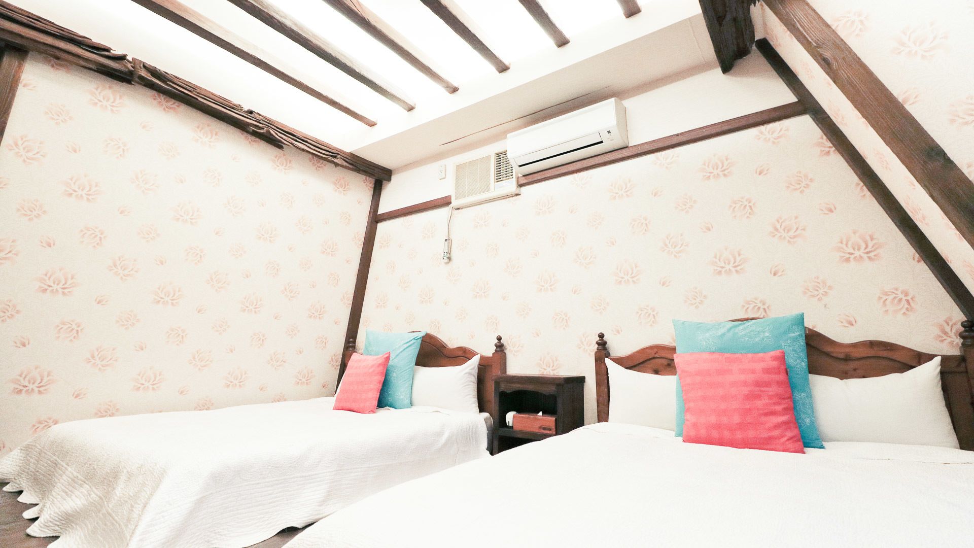 Un dormitorio con dos camas, un tragaluz, aire acondicionado y papel tapiz floral.