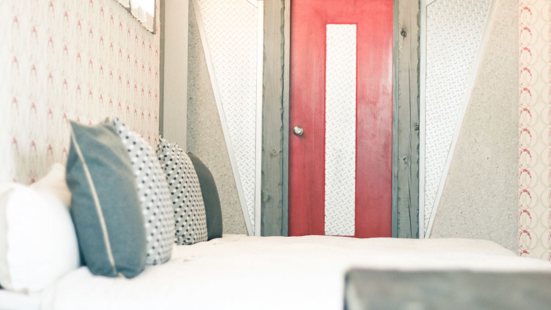 Una cama con almohadas y una puerta roja al fondo.